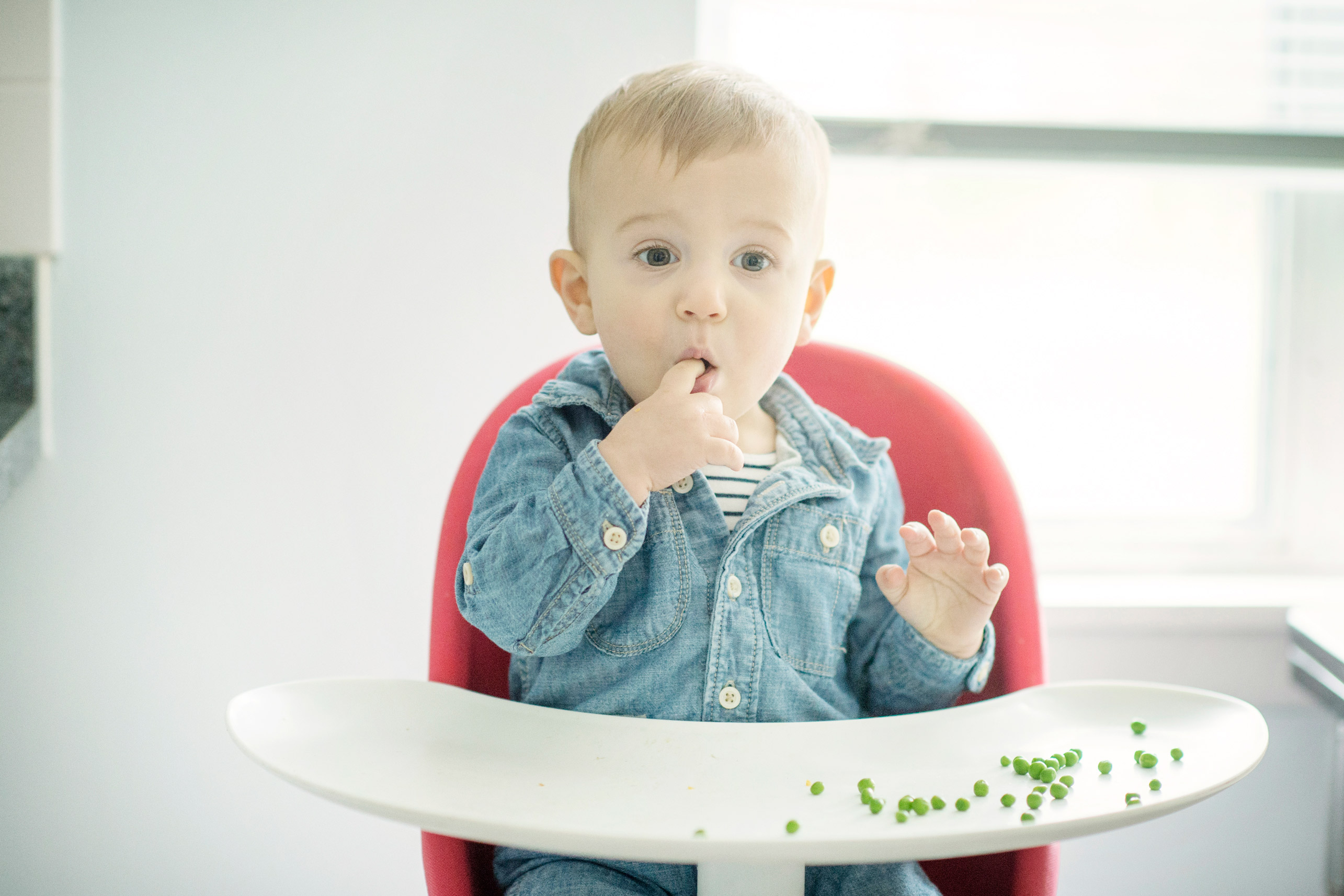 toddler eating peas in high chair